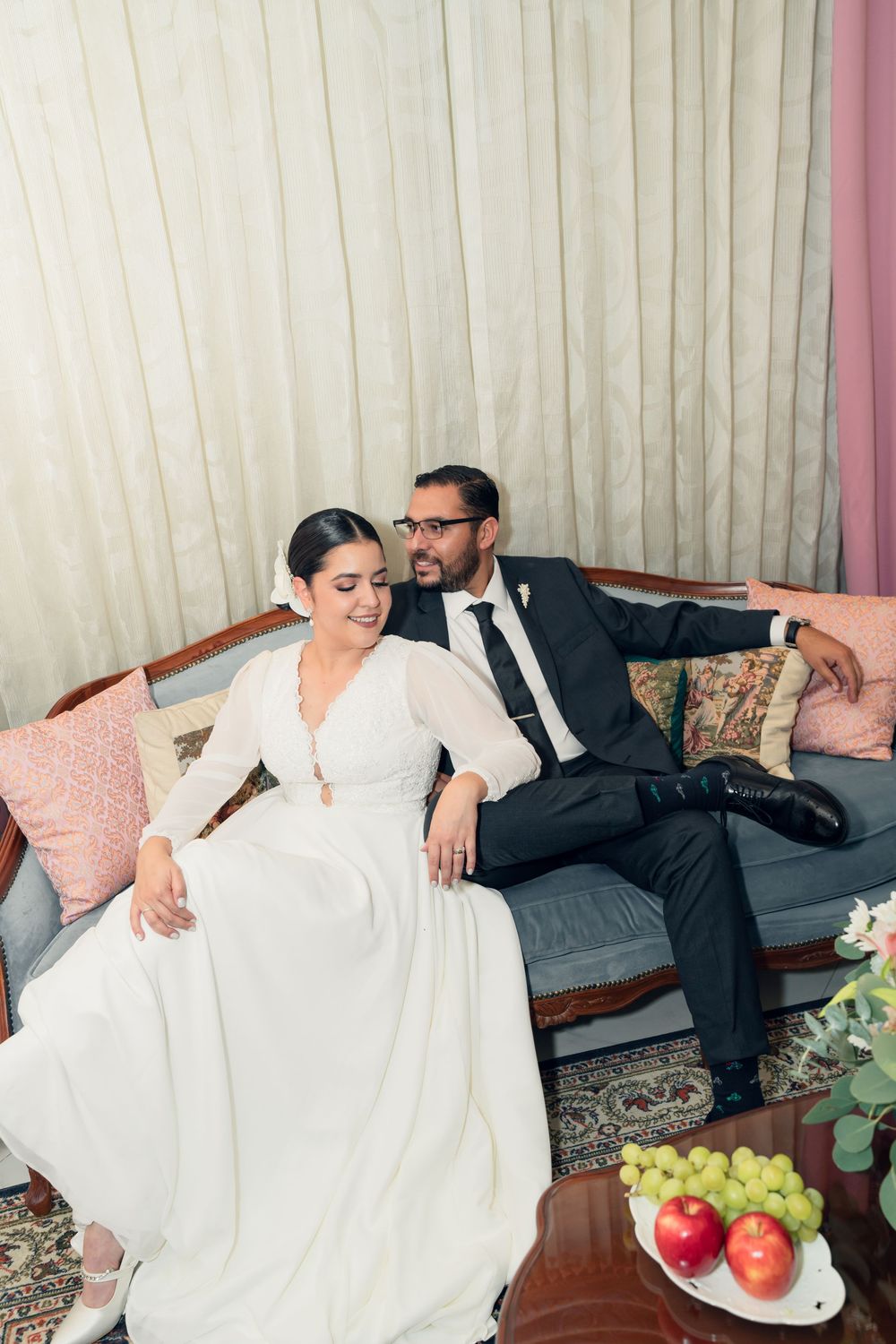 Wedding couple relaxing on vintage sofa with fruit and decorative pillows.
