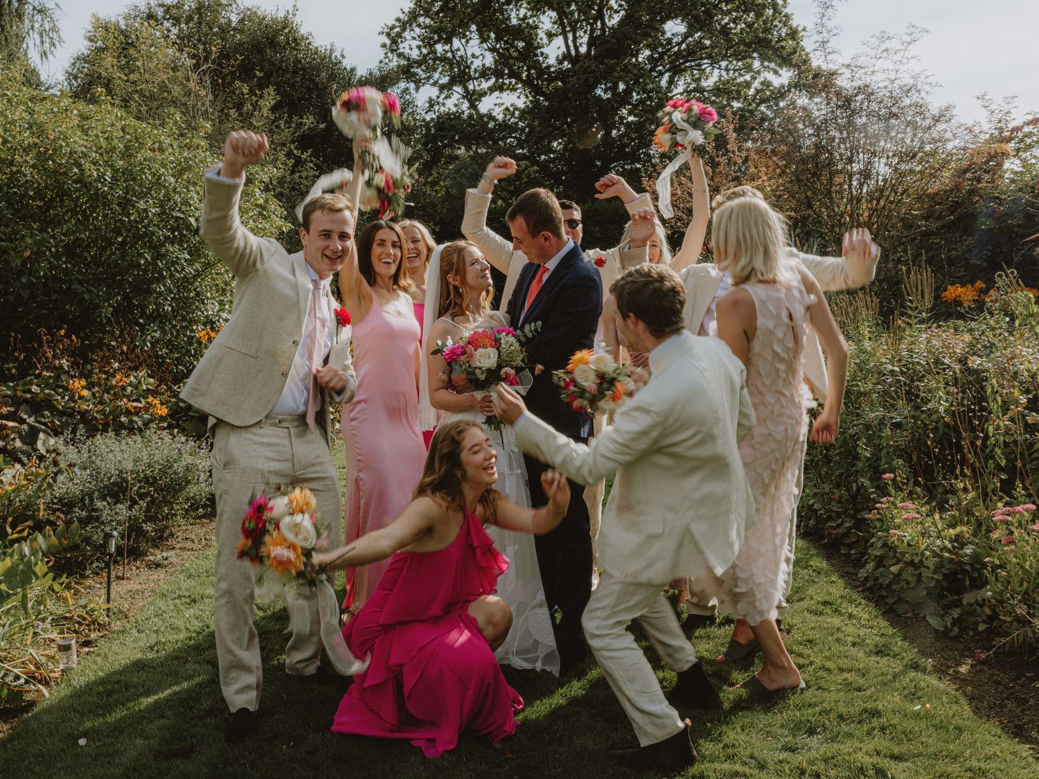 Wedding party celebrates joyfully on a grassy lawn during an outdoor summer celebration.