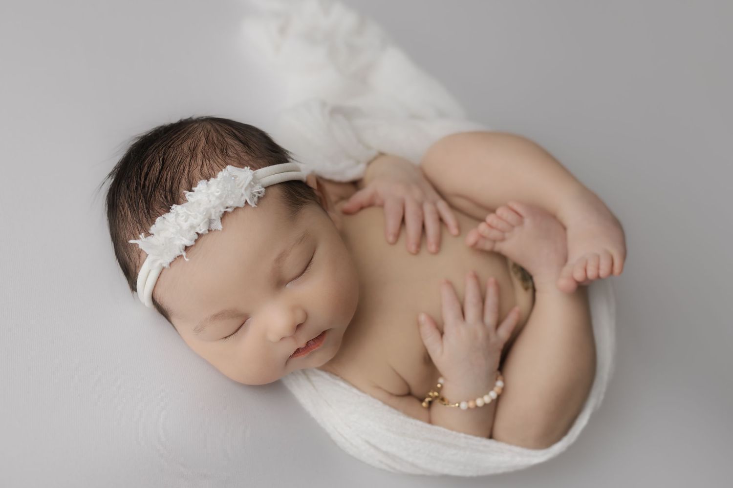 Sweet sleeping baby girl swaddled in a white wrap on a while simple backdrop blanket for her newborn studio session.