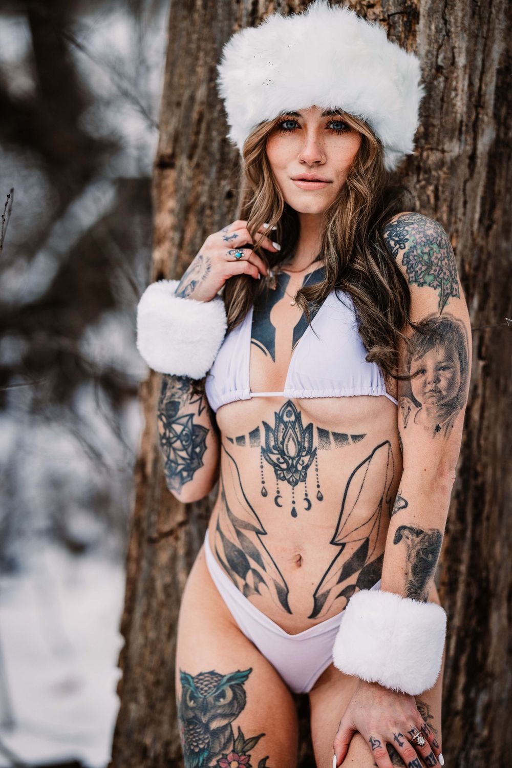 Winter portrait with white fur hat and lingerie showcasing ornate tattoo artwork.