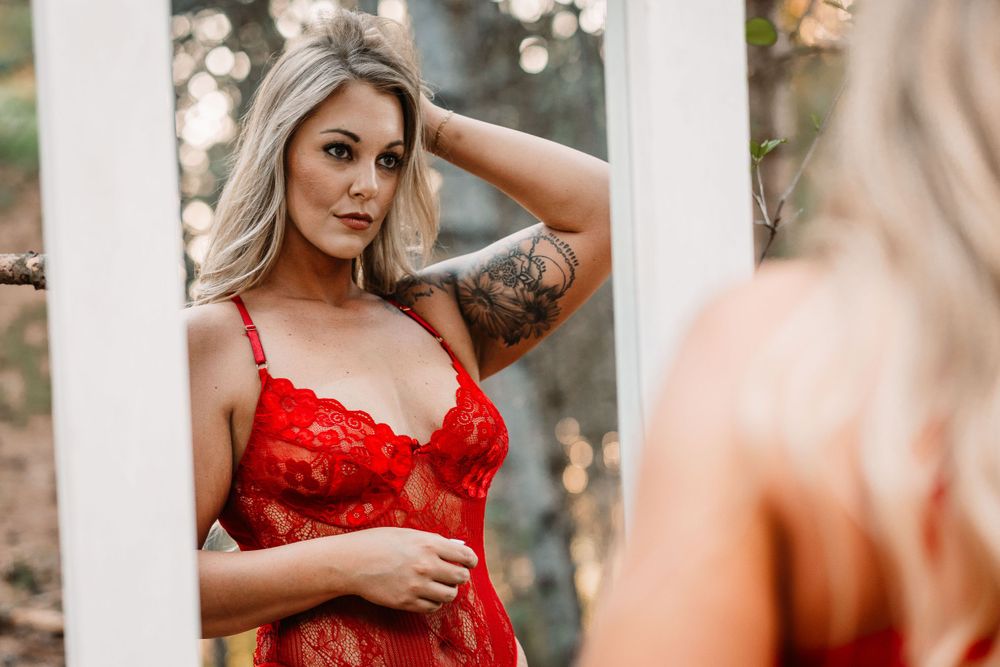 Reflective fashion portrait in red lingerie with mirror in outdoor garden setting.