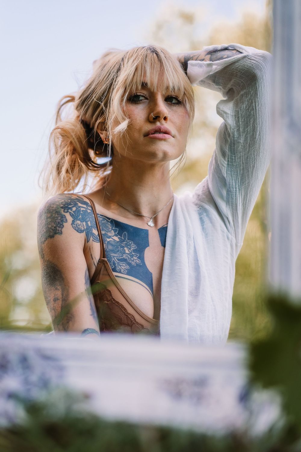 Portrait of woman with tattoos wearing white sweater in soft natural lighting.