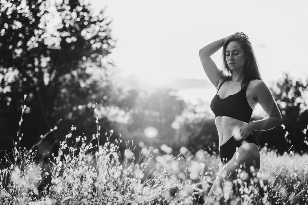 Silhouette of person in athletic wear poses among wildflowers at sunset.