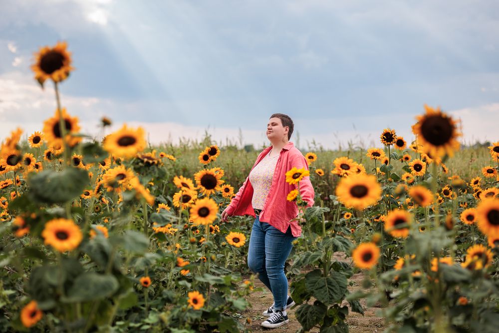 Person in coral shirt exploring a scenic sunflower field during golden hour at Tuttle Orchards.