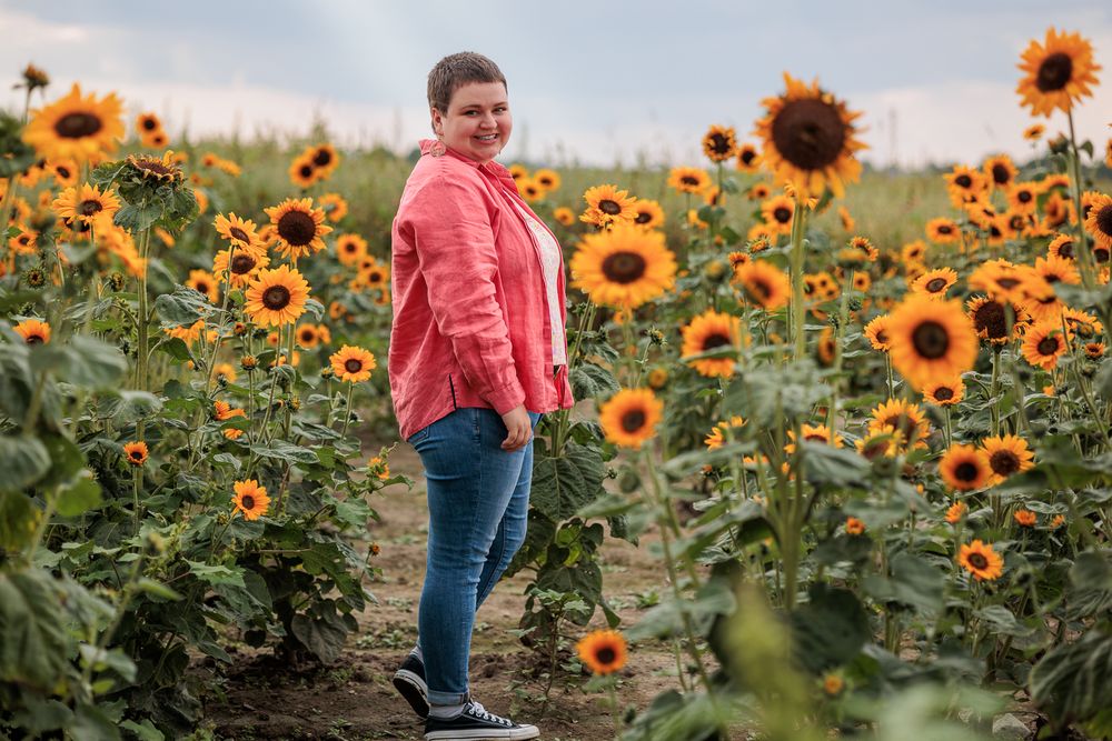 Person in pink top and jeans walking through a vibrant field of tall blooming sunflowers on a sunny day.