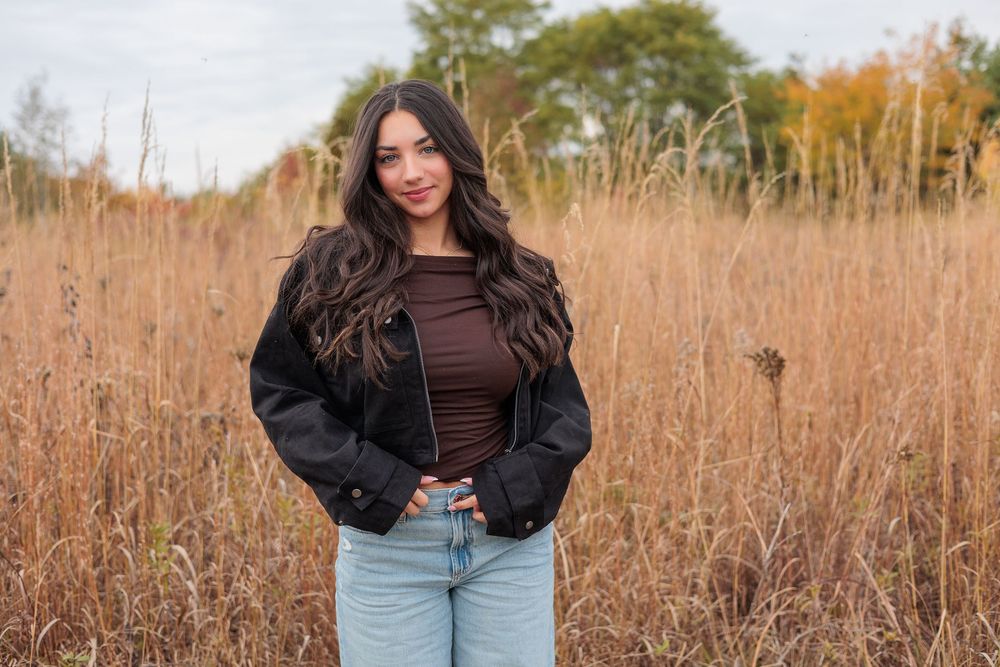 Beautiful young women poses outdoors in a brown shirt and jeans against tall autumn grass during golden hour at Beckenholdt Park