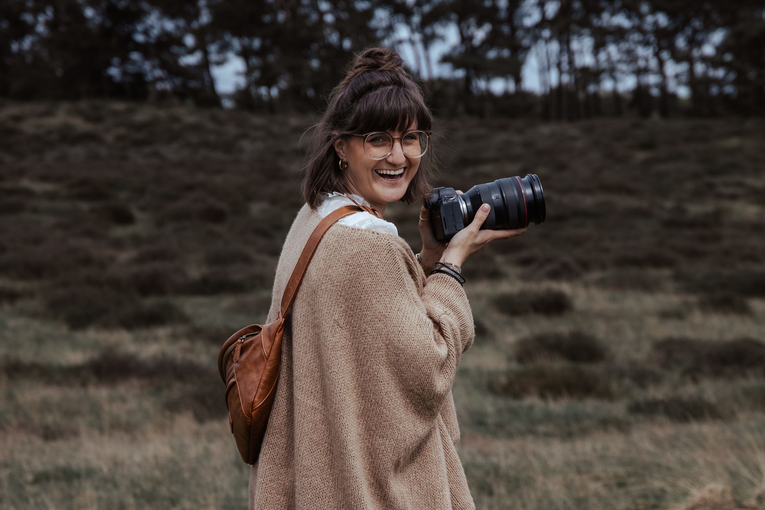 Person wearing beige sweater photographing outdoors in natural landscape.