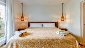 Cozy bedroom with a king-size bed, golden bedspread, folded towels, and warm pendant lights flanking a white headboard.