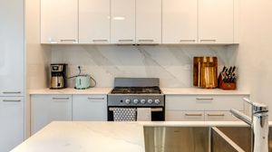 Modern white kitchen with marble backsplash, stainless steel gas range, white cabinetry, and quartz countertops.