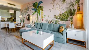 Modern living room with teal sofa, white coffee table, and tropical floral mural wallpaper in bright, airy space.