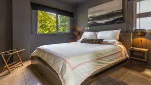 Modern bedroom interior with gray walls, wooden floors and large windows offering natural light and scenic views.