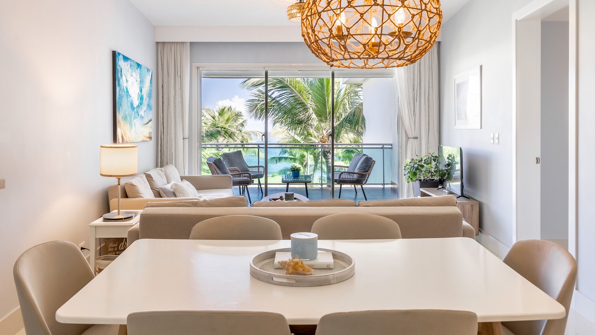 Modern coastal apartment interior with open floor plan featuring white decor, geometric pendant light and ocean views.