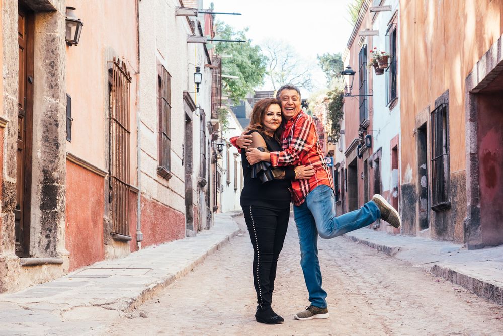 Couple embracing while walking down a charming cobblestone street in Mexico with colorful colonial buildings.