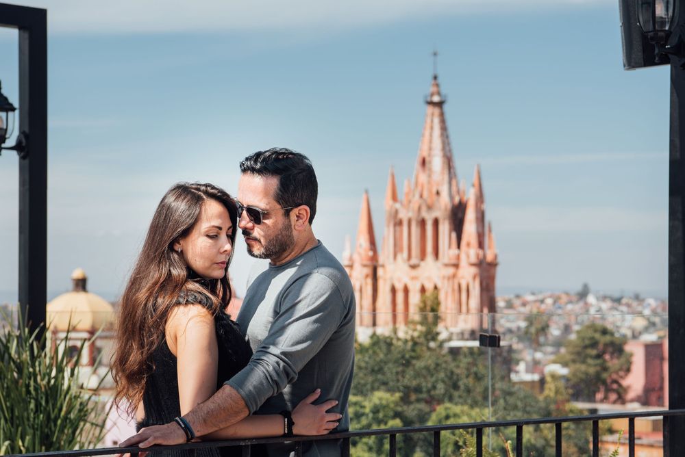 A romantic couple embraces on a balcony overlooking the pink Parroquia church in San Miguel de Allende, Mexico.