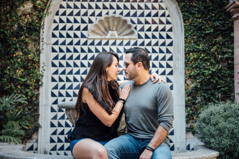 A couple shares an intimate moment while sitting in front of a decorative geometric patterned archway surrounded by greenery.