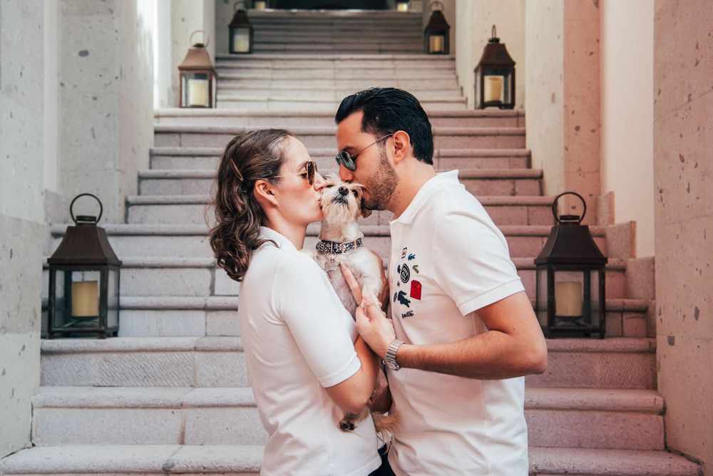 A couple in white outfits shares a romantic moment on pink marble steps with lanterns in the background.