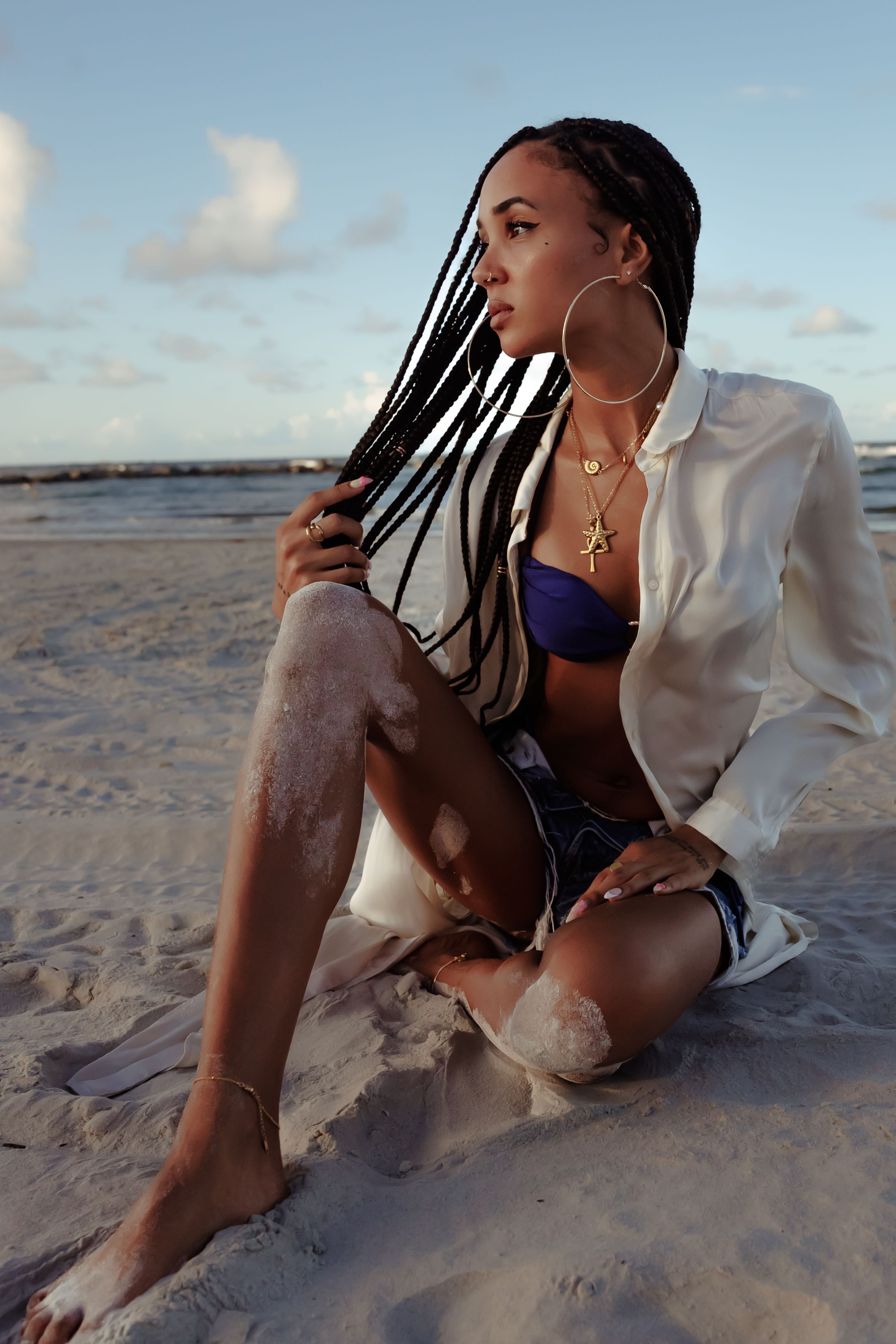 Fashion portrait on beach with white blazer and statement jewelry at golden hour.