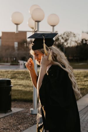 Graduate in cap and gown posing outdoors at sunset with glowing globe lights in the background.