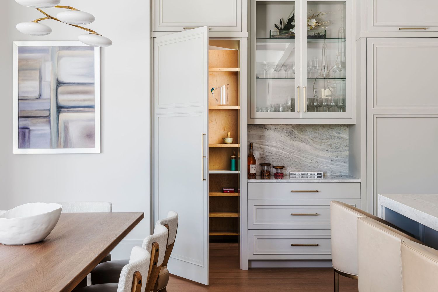 Modern kitchen with gray cabinetry, open pantry, marble backsplash, glass-front cabinets, and warm wood dining table.