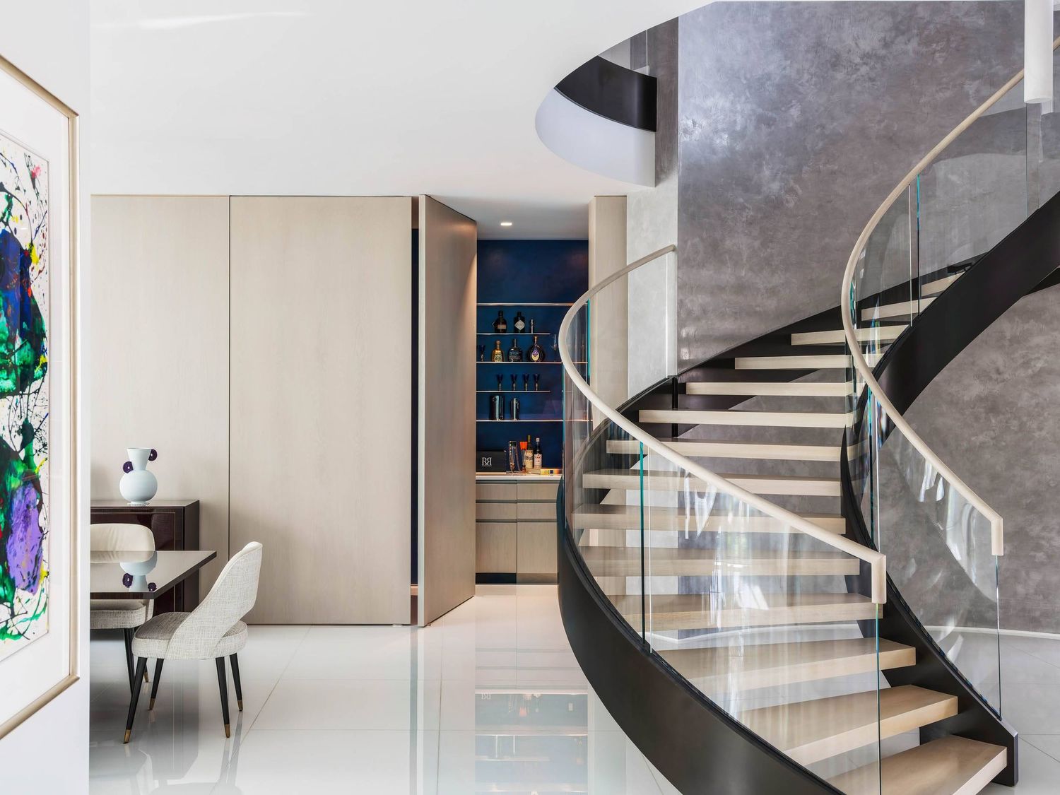 Contemporary interior featuring a curved spiral staircase with glass railings and abstract wall art.