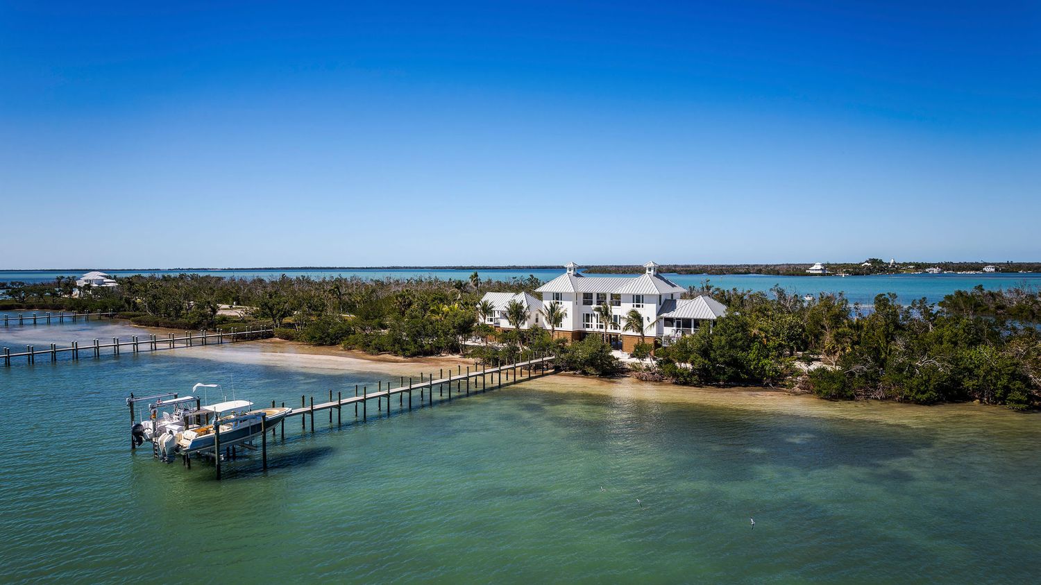 Aerial view of a luxury waterfront estate on a private island with a dock, turquoise waters, and lush tropical landscaping.