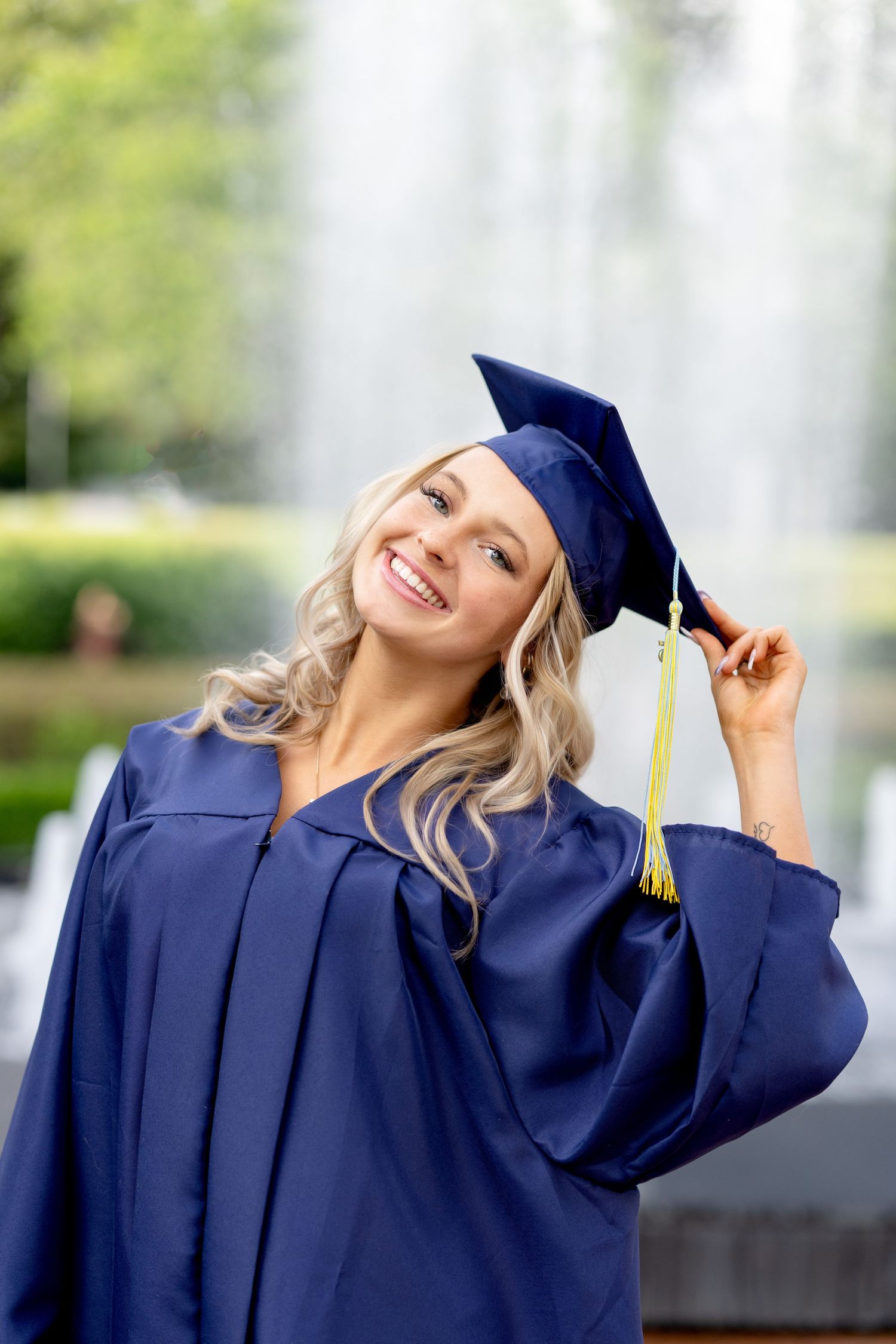 Woman in white dress poses near cascading outdoor fountain holding blue purse.