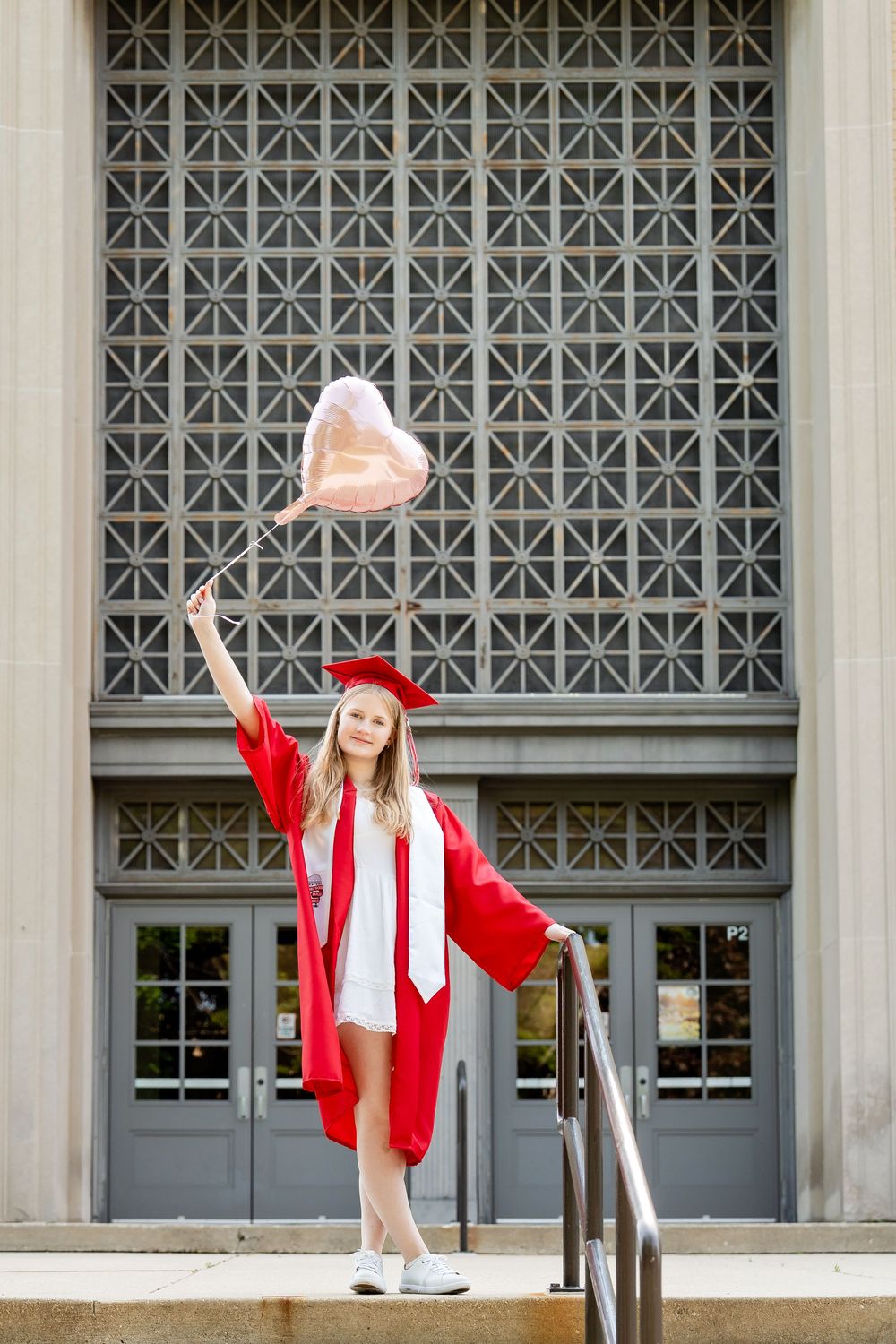A graduate in regalia holding a balloon on the top of a staircase at a school taken by Milwaukee senior photographer Rachel Dickman.
