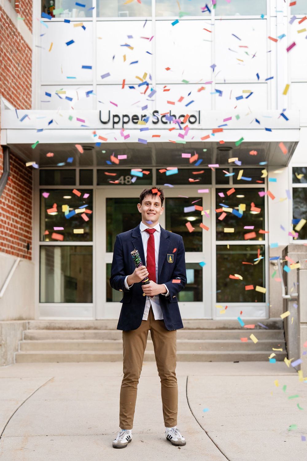 A graduate popping a confetti cannon in front of a building at a school taken by Milwaukee photographer Rachel Dickman.