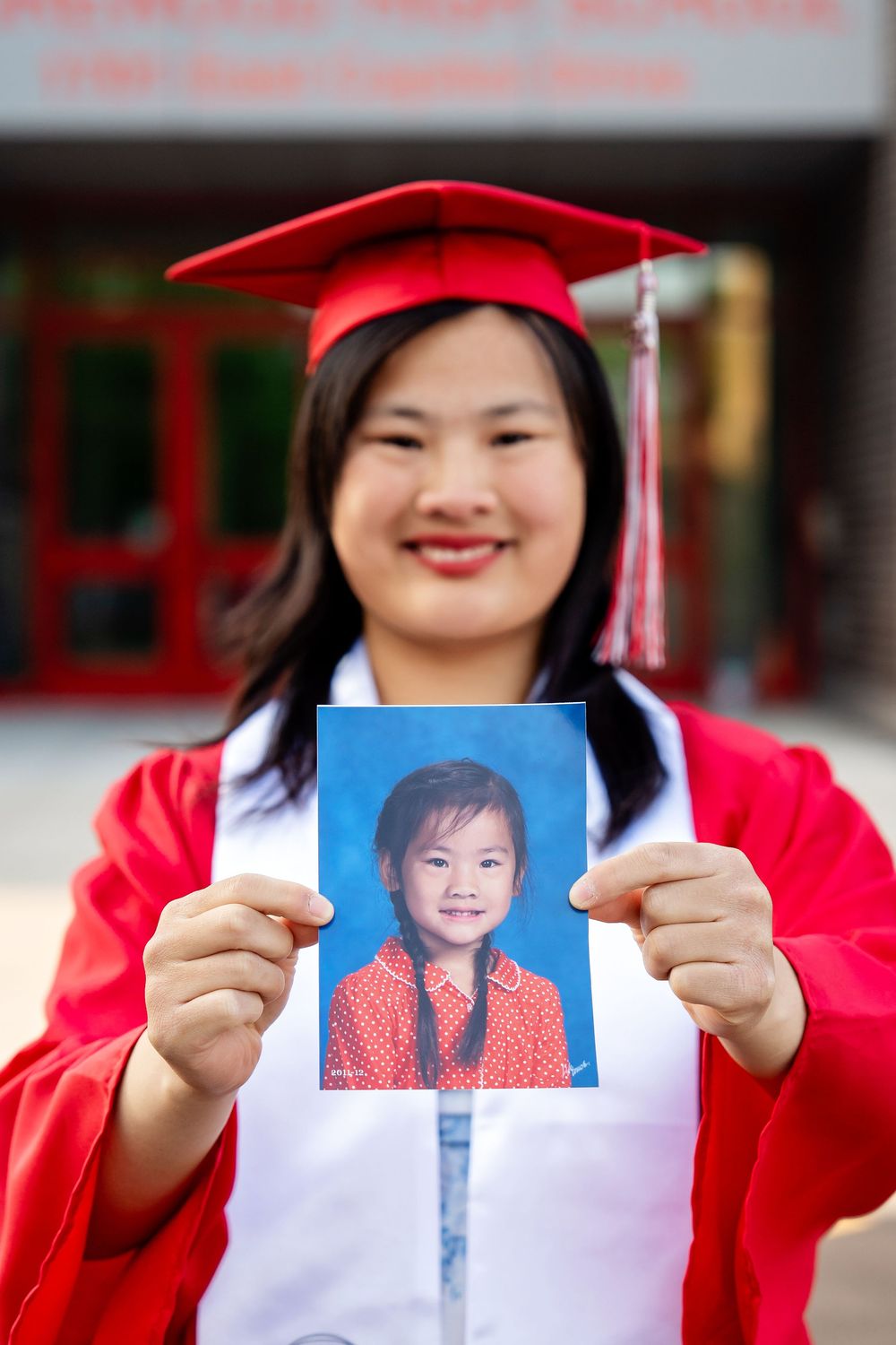 A graduate in regalia holding a a kindergarten photo of herself at a school taken by Milwaukee senior photographer Rachel Dickman.