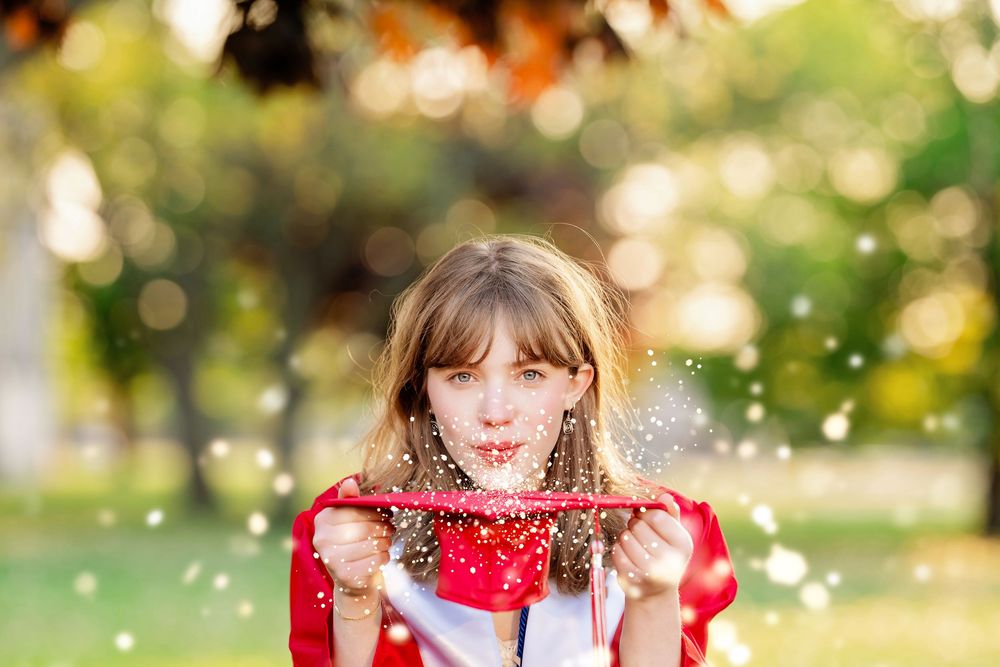 A graduate blowing glitter off her graduation cap with sparkly trees in the background taken by Milwaukee senior photographer Rachel Dickman