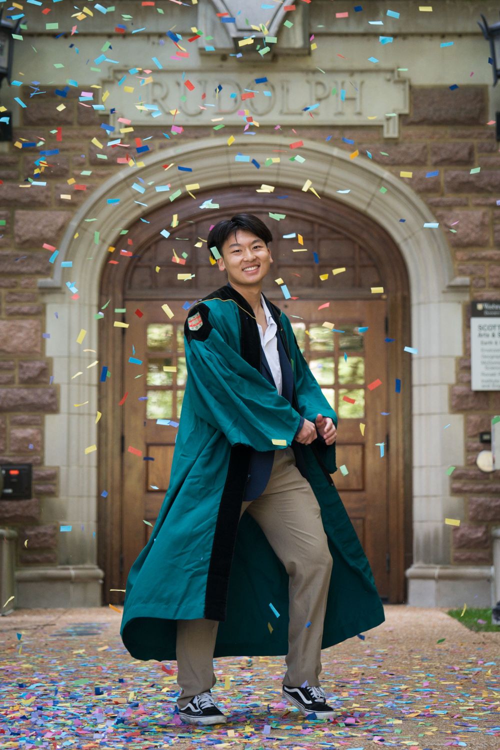 Graduation photo of man in green gown smiling, confetti in the air - shot by Milwaukee event and graduation photographer Rachel Dickman.