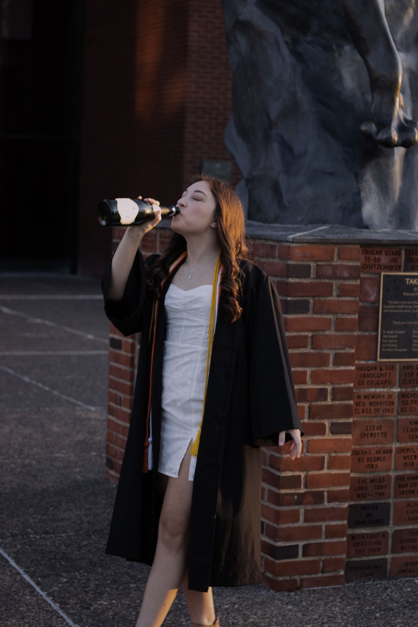 A woman drinking champagne outside on graduation day