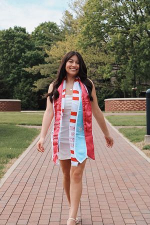 Young woman walking down a brick path smiling into the distance on her graduation day