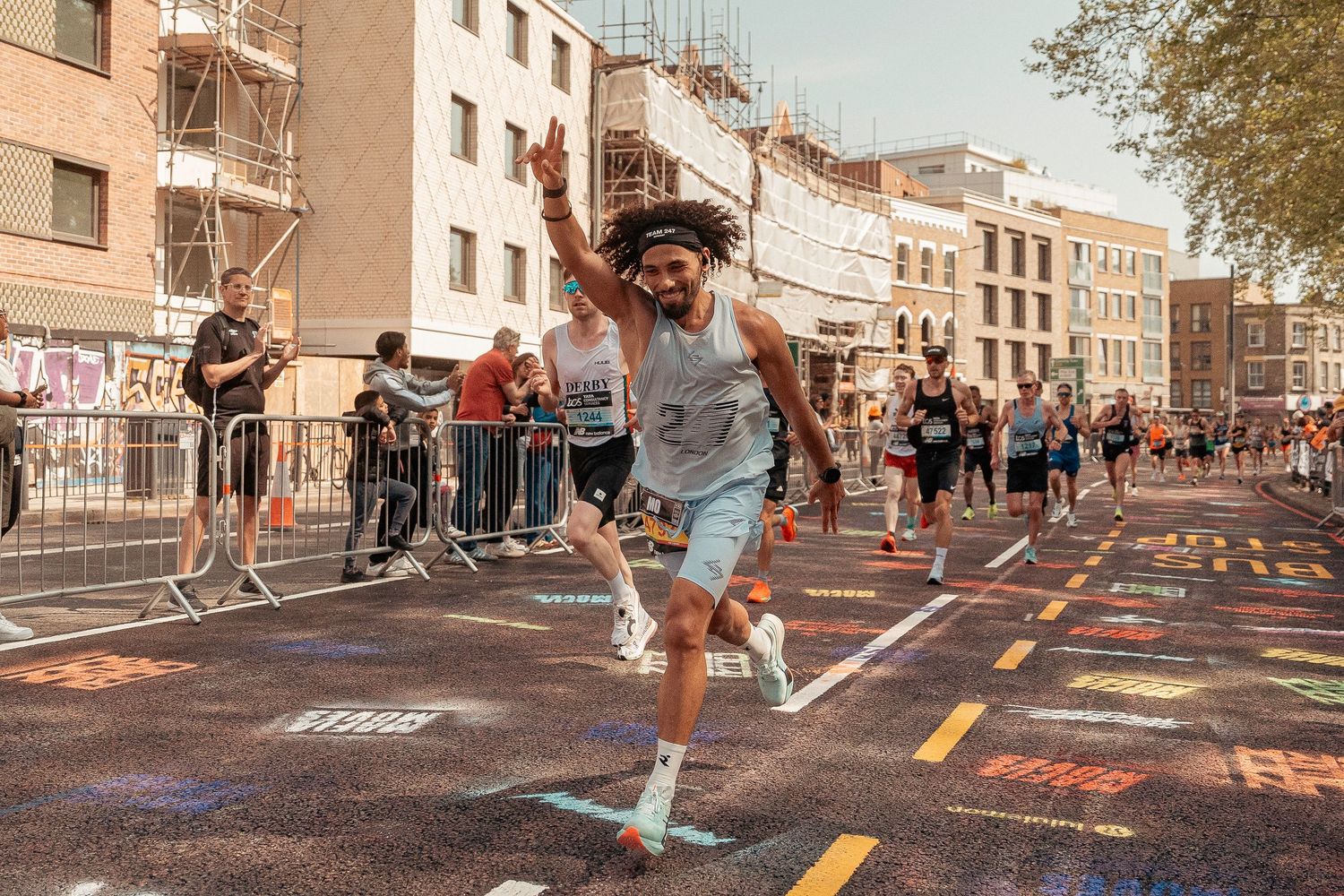 Runner joyfully jumps during a marathon race on a city street lined with spectators and buildings on a sunny day.