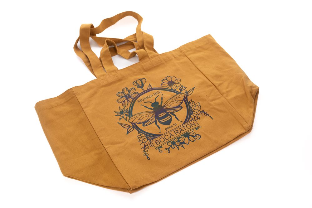 Tan canvas tote bag with decorative bee and floral design printed in black ink.