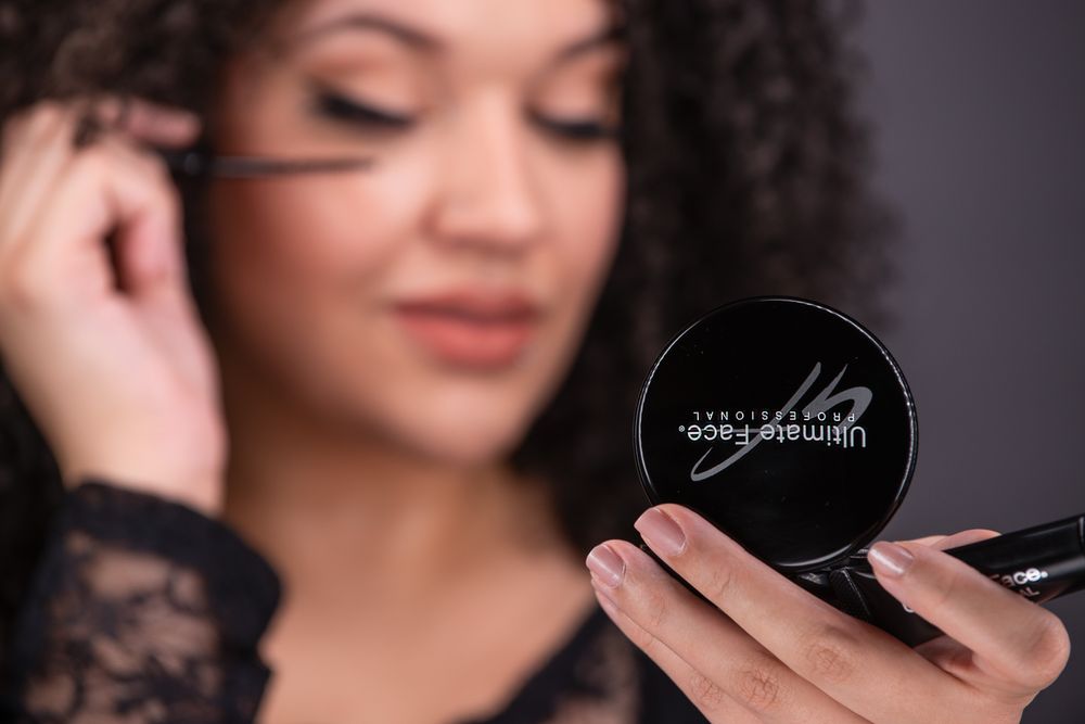 Person wearing lace holding a circular makeup compact while looking down with soft lighting.