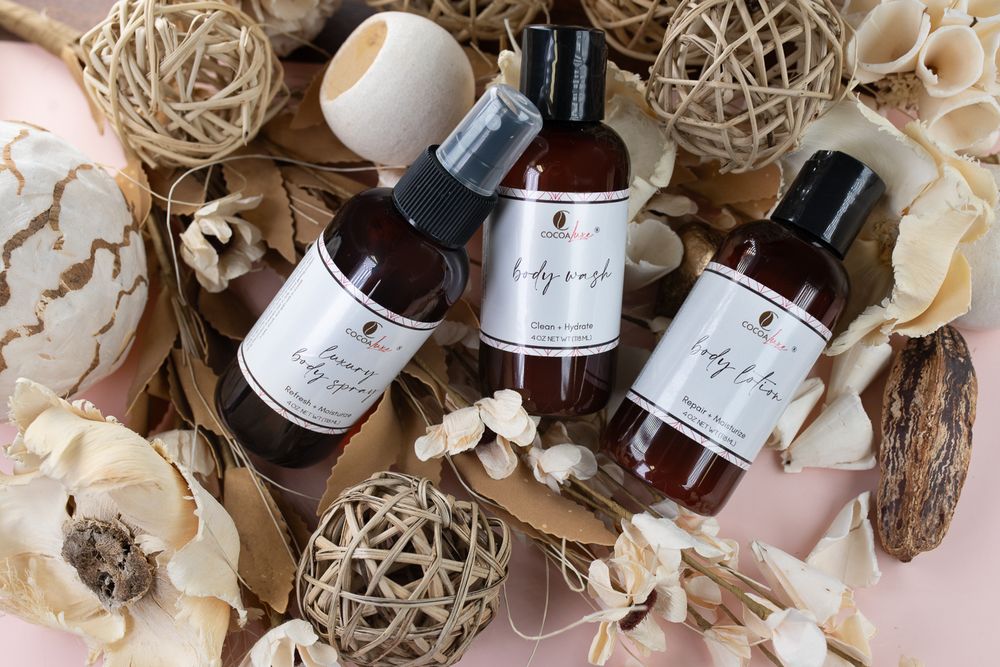 Luxury brown glass beauty product bottles arranged with decorative woven spheres and dried floral elements on neutral surface.