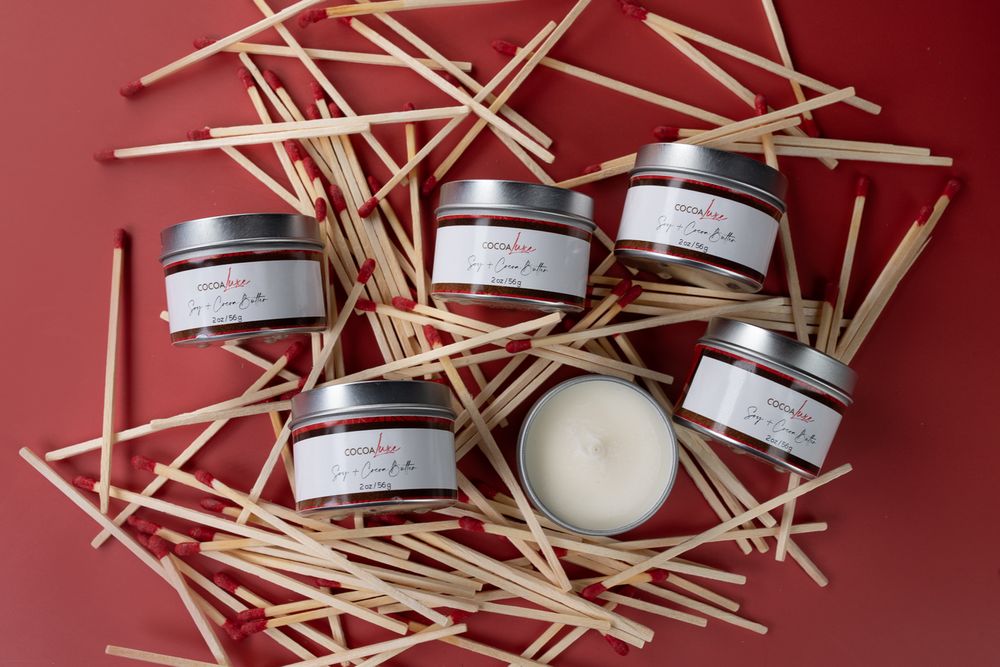 Six small tin candle containers arranged on scattered wooden matchsticks against a red background.