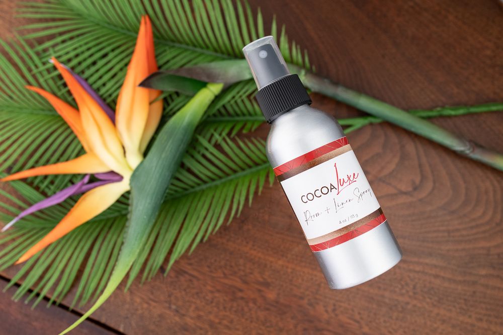 White coconut hair mist bottle on wooden surface with tropical bird of paradise flower and palm leaf.