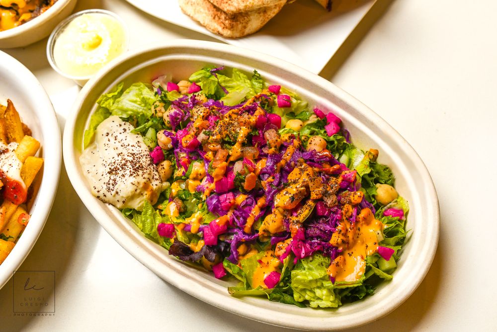 Colorful salad bowl with roasted chicken, lettuce, red cabbage, corn and seeds on white table.