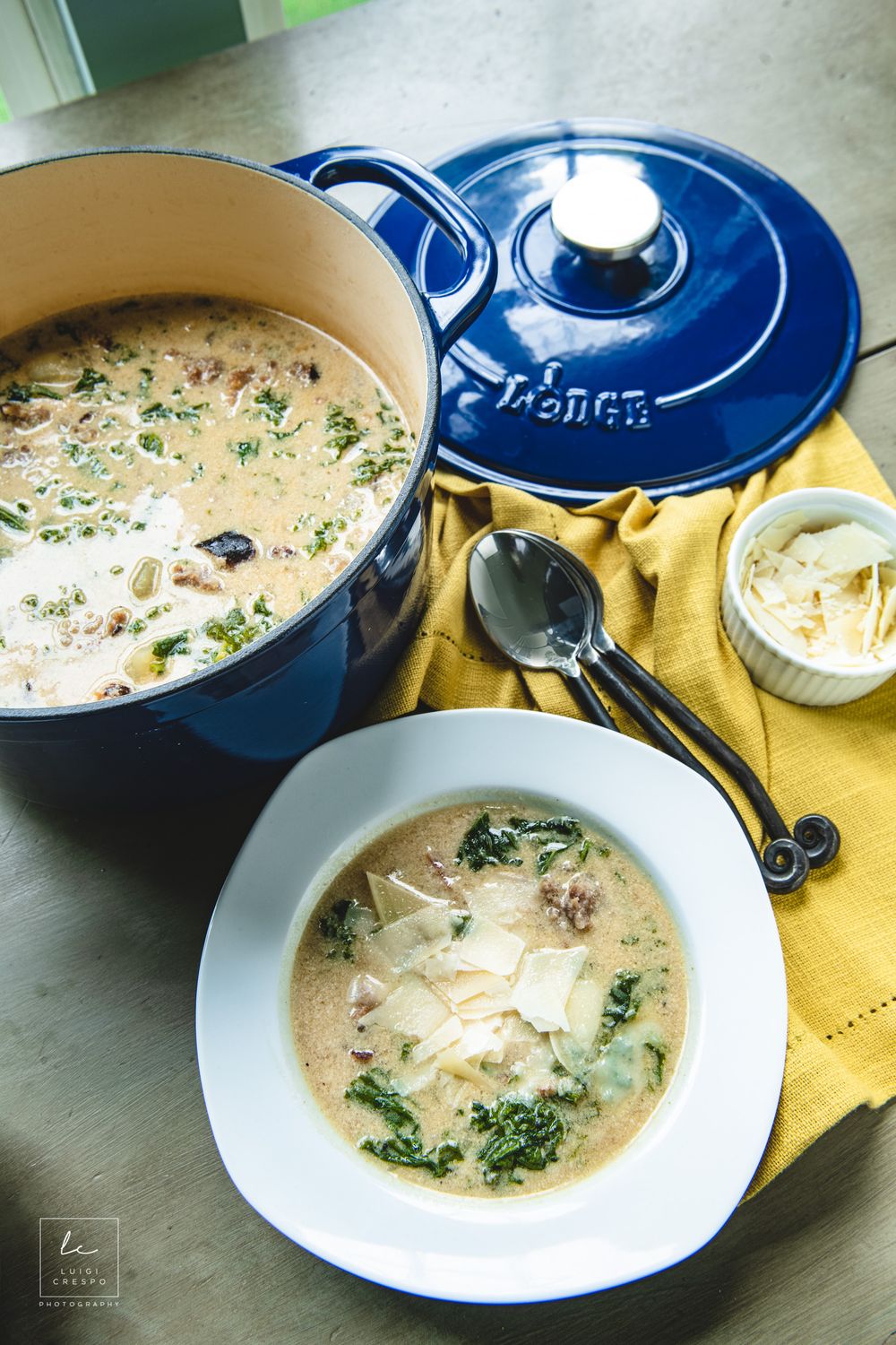 A bowl of creamy Tuscan soup with kale and sausage served in a blue Dutch oven pot with a yellow napkin.