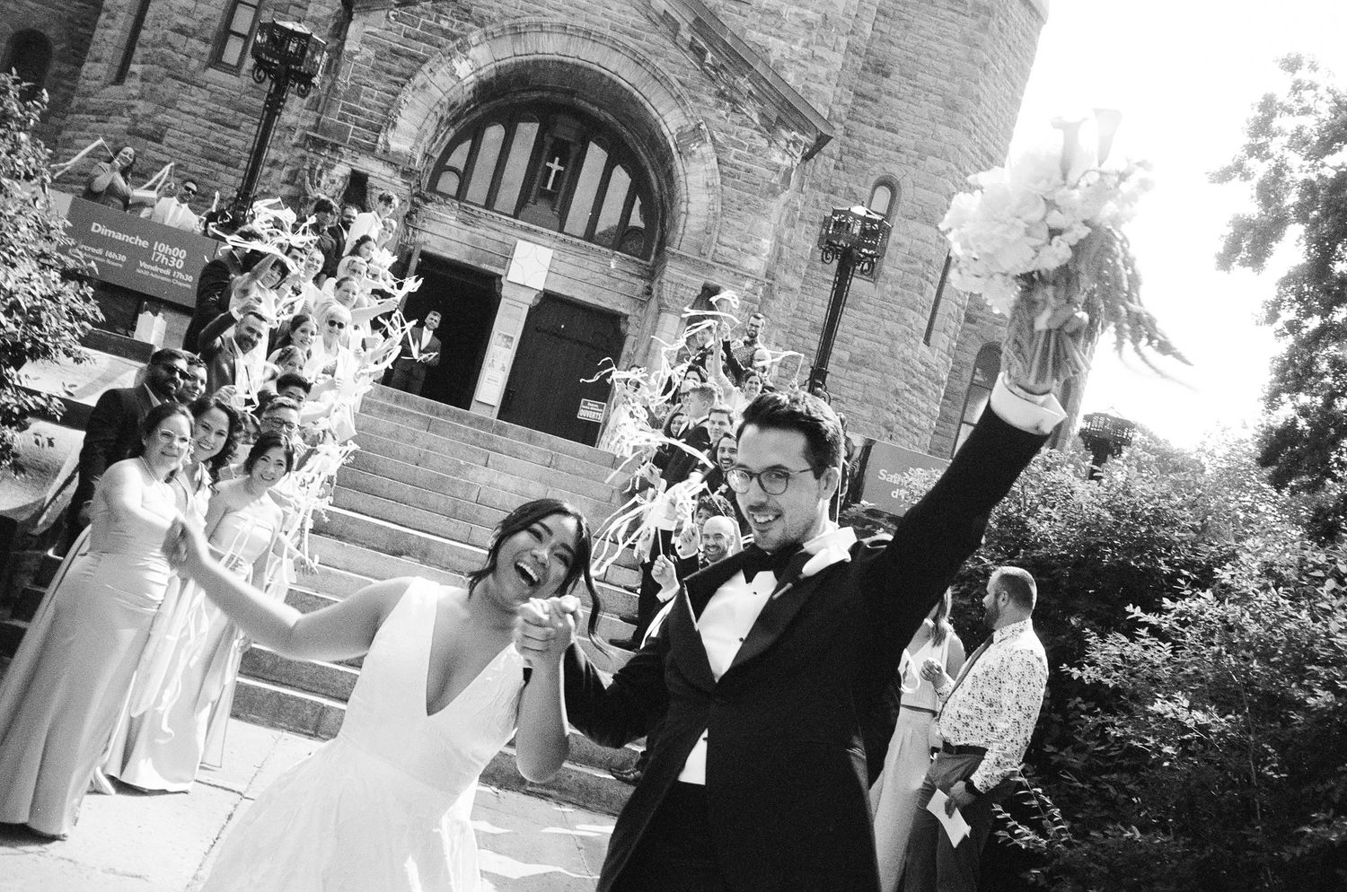 A collection of candid black and white wedding photos showing guests and celebrations outside a stone building.