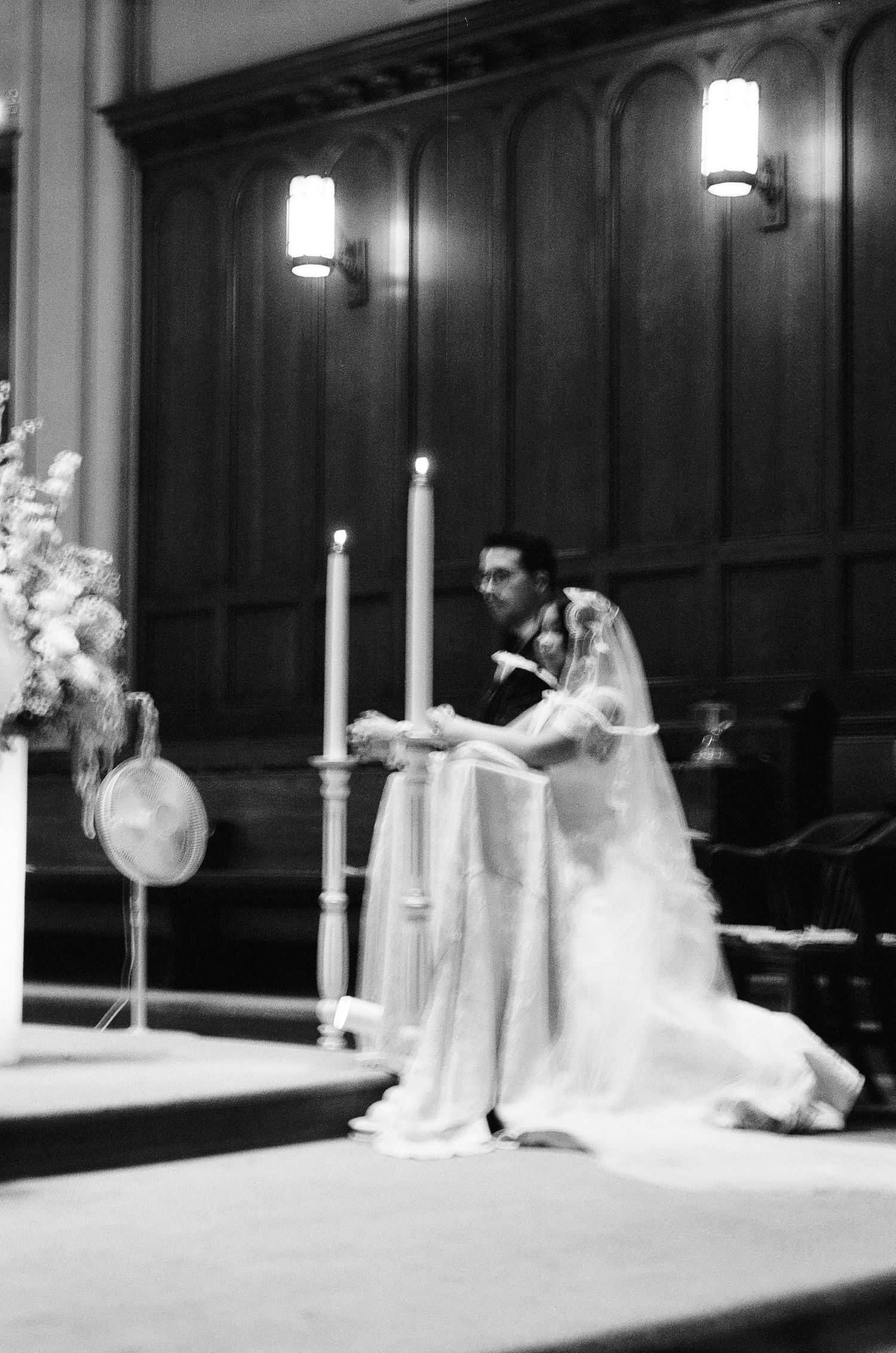 Wedding ceremony scene inside a dark wood-paneled church with candles and floral arrangements.