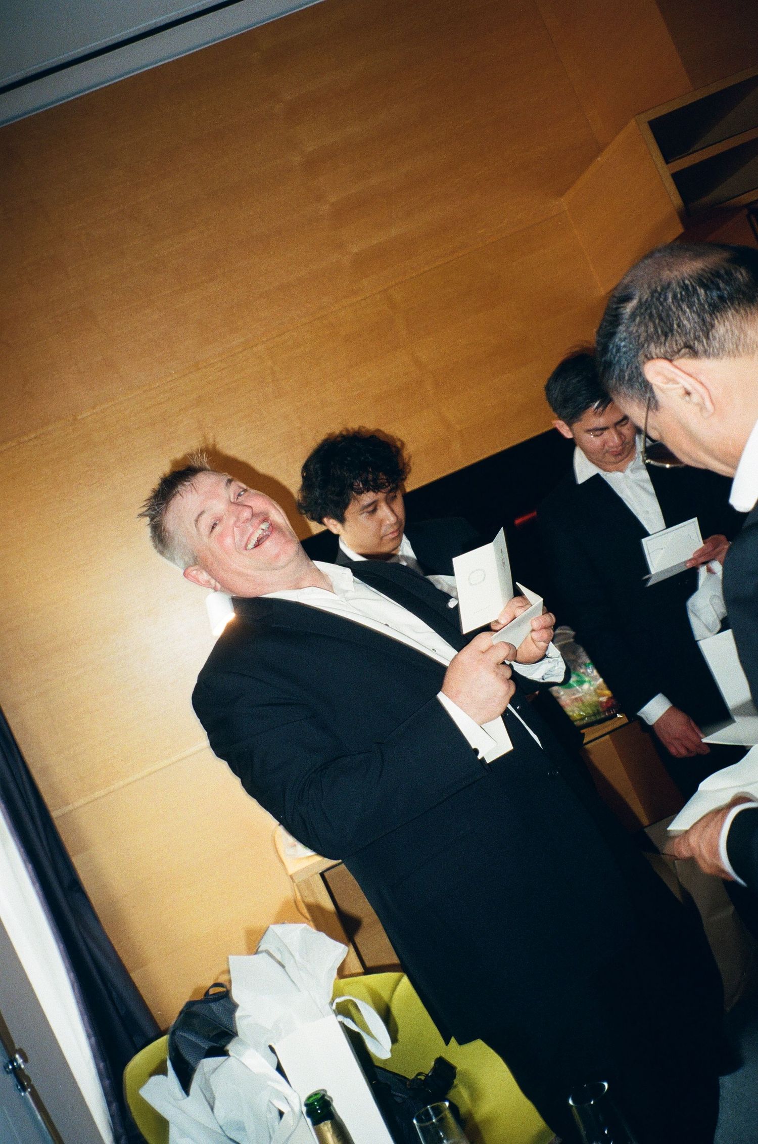 Multiple sequential photos showing people in formal attire laughing and interacting at an indoor event.