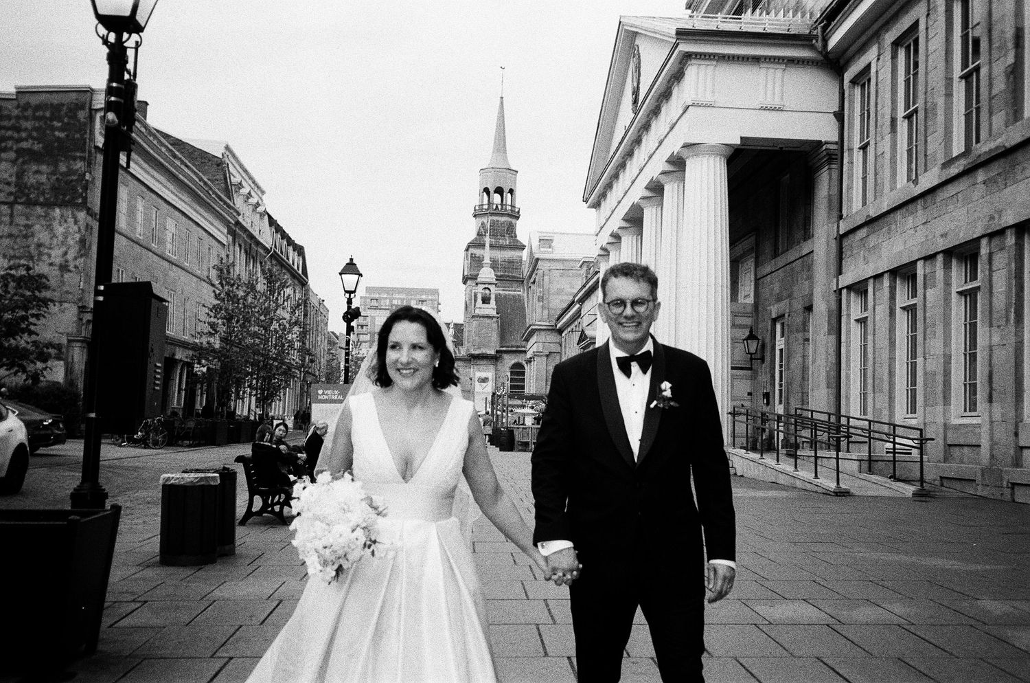 Black and white wedding photos showing a couple walking together on a cobblestone street with church spires in background.