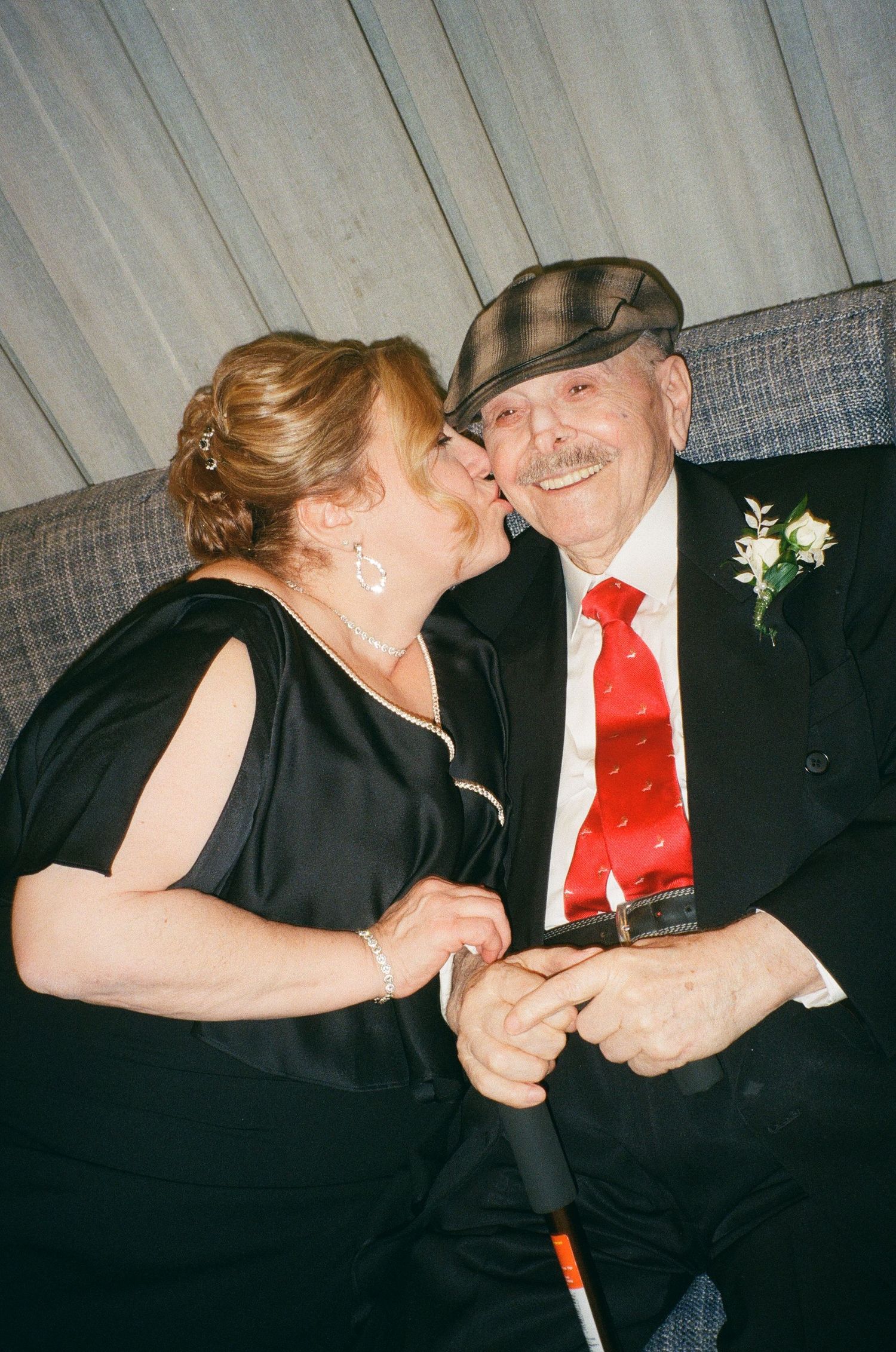 A couple in formal black attire share a tender moment while dancing together at an event.