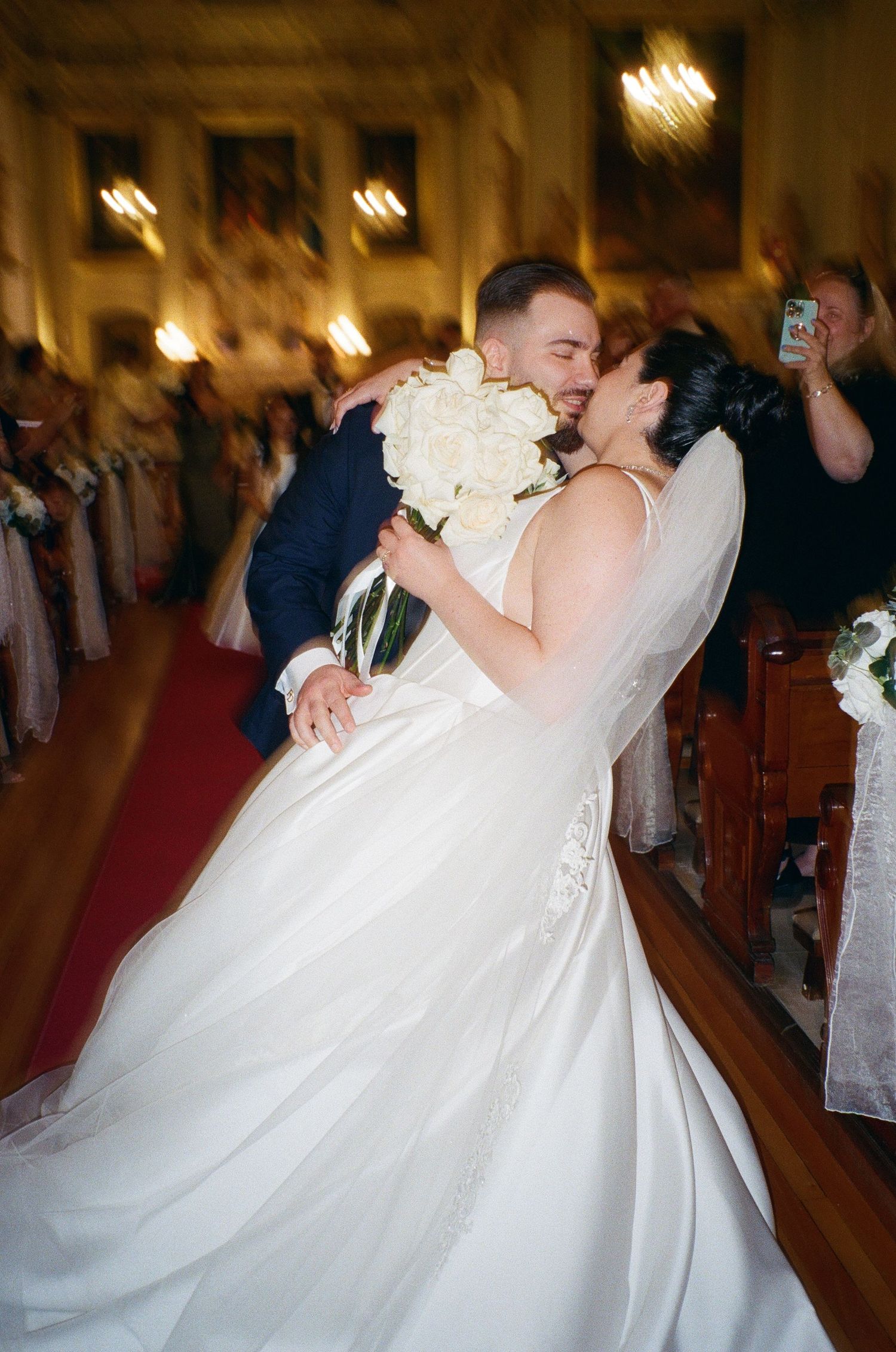 Wedding couple dancing together in a dimly lit ballroom with guests watching in the background.