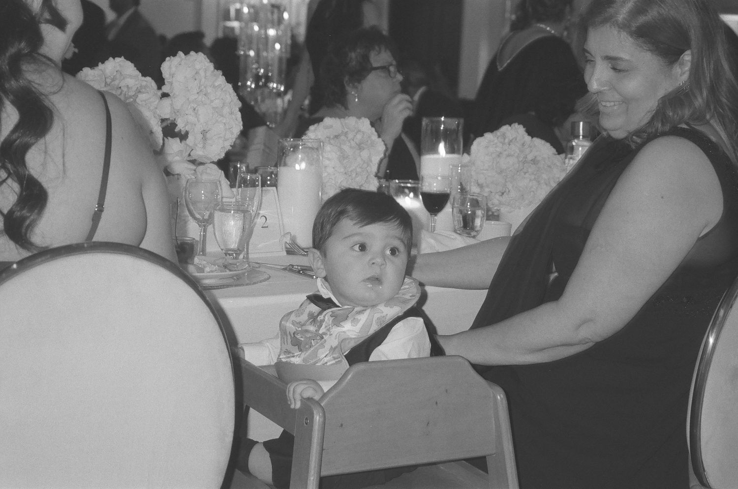 Wedding reception guests seated at elegant tables with white linens and crystal chandeliers overhead.