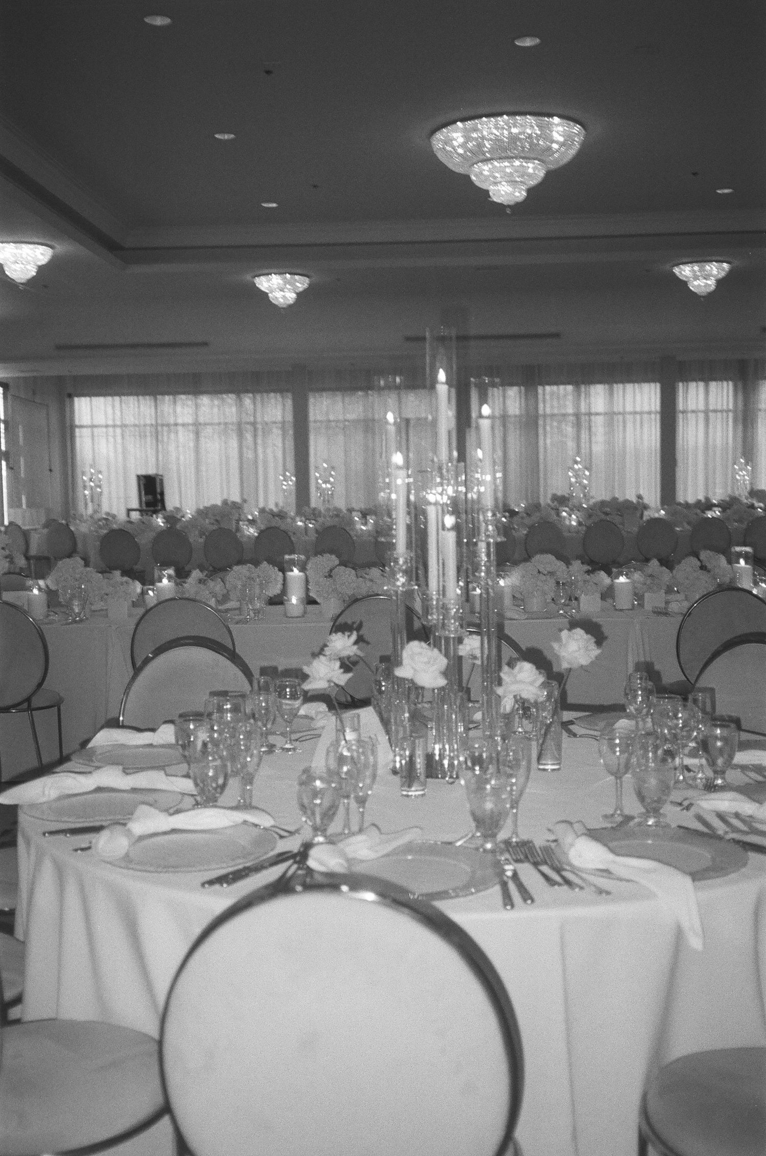 Elegant banquet hall setup with round tables covered in white linens and crystal chandeliers hanging from the ceiling.