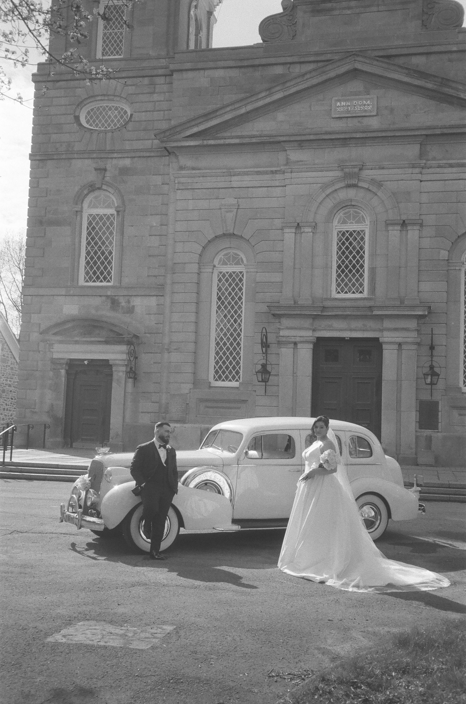 Classic vintage car parked in front of a stone church building with latticed windows.